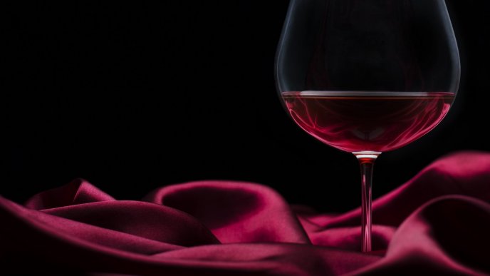 A glass with red wine on a burgundy silk