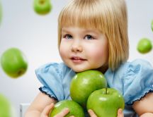 A sweet girl in blue with many green apples in her arms