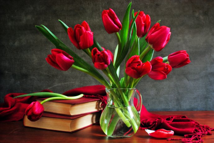 A bouquet of red tulips in a vase next to some books