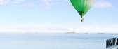 A green air balloon flies over the sea