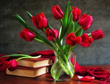 A bouquet of red tulips in a vase next to some books