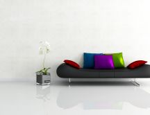 A black sofa with colorful pillows beside a flower