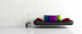A black sofa with colorful pillows beside a flower